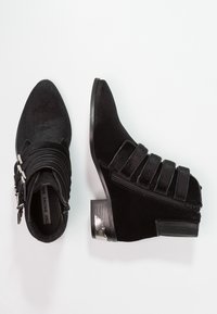 Stivaletti neri alla caviglia in suede con punta affusolata, caratterizzati da molteplici cinturini, una zip laterale e un accent metallico sul tallone.