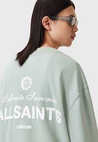 Sudadera oversized verde menta con texto impreso en blanco "Infinite Summer ALLSAINTS LONDON" en la parte posterior y cuello acanalado.
