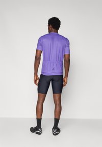 T-shirt de sport violet à manches courtes avec un design ajusté, associé à un short de cyclisme noir. Comprend une poche arrière et des détails de logo.