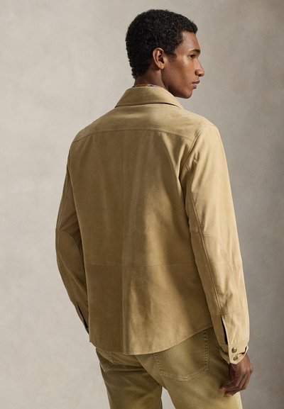 Μπεζ σατέν ζακέτα με γιακά, μακριά μανίκια και κουμπωτά μανσέτα. Διαθέτει ορατές ραφές και άνετη γραμμή.