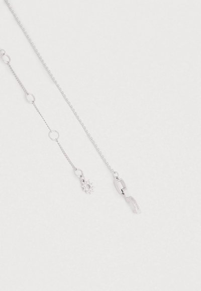 Colar de corrente prateada com um pendente em forma de explosão de estrela, um elo texturizado e um fecho seguro. O design é minimalista e subtil.