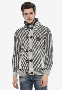 Gebreide cardigan in een zwart-wit visgraatpatroon, met een hoge kraag, sluitingen met toggles en voorzakken. Textuurstof.