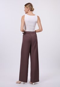Hvit tettsittende tank topp parret med vide brune bukser med snor i livet og baklommer. Glatt stoff med minimal tekstur.