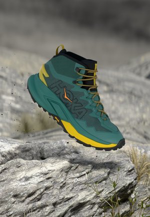 Chaussure de randonnée en vert et jaune, avec une tige texturée, des semelles robustes, et un col haut. Remarquable pour son design léger.