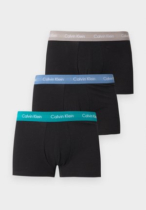 Τρία μαύρα ανδρικά μπόξερ με λάστιχο μέσης Calvin Klein σε γκρι, μπλε και τιρκουάζ, τοποθετημένα στοιβαγμένα σε λευκό φόντο.