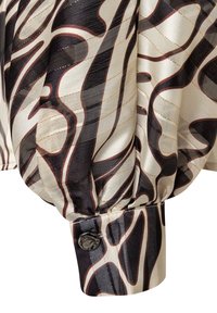 Rękaw satynowej bluzki z wirującym czarno-beżowym wzorem, marszczoną fakturą i czarnym guzikiem przy mankiecie.