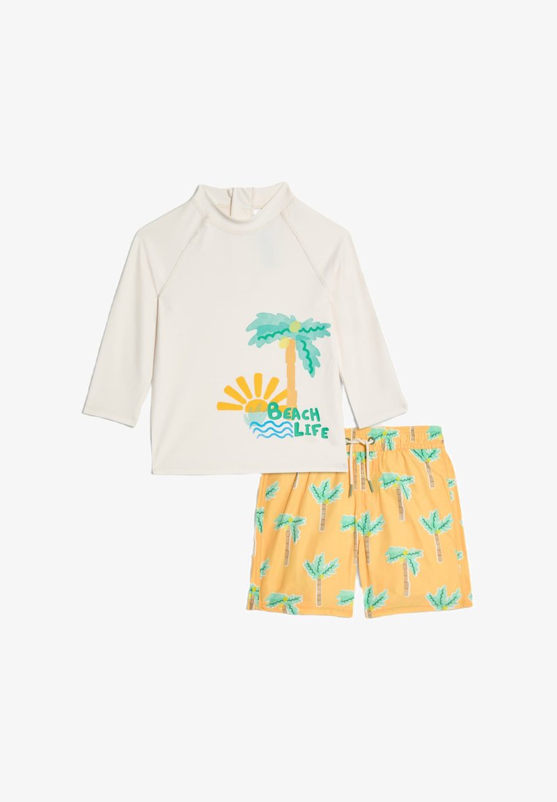 Rash guard blanco con gráfico de palmera y texto "Vida de Playa", combinado con pantalones de baño amarillos con patrones de palmeras verdes.