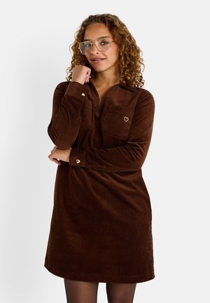 Robe chemise en velours côtelé marron avec deux poches poitrine, accents en forme de cœur dorés sur les poches et les poignets, et une coupe décontractée, avec un devant à boutons.