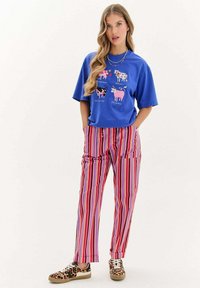 Modrá triko s krátkým rukávem a barevným grafikou krávy; růžové a fialové pruhované kalhoty; tenisky se zvířecím vzorem. Neformální outfit s živými vzory.