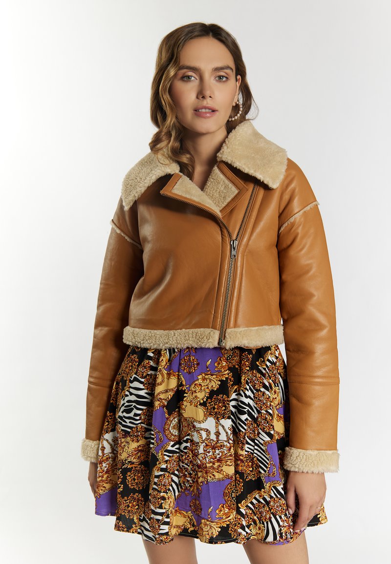 Brun læder cropped jakke med faux pels krave og manchetter. Båret over en sort og lilla mønstret nederdel med dyreprints og ornamentale designs.