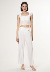 Witte cropped top met oogjes borduurwerk en gerimpelde banden, gecombineerd met losse witte broeken met een tekstuurtailleband.