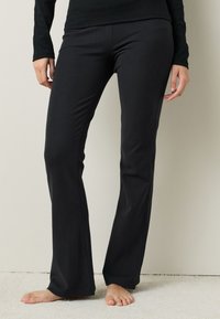 Pantalones de yoga negros acampanados hechos de tela elástica. Textura suave, sin patrones visibles, y una cinturilla que se ajusta cómodamente a las caderas.