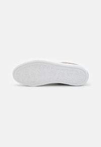 Sola di sneaker bianca con gomma testurizzata, marchio "GUESS" stampato, design piatto, leggera curvatura nella punta, aspetto pulito e semplice.