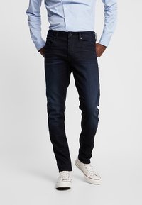 Mörkblå denimjeans med slim fit, med framfickor och en ren design. Matchas med vita sneakers och en ljusblå skjorta.