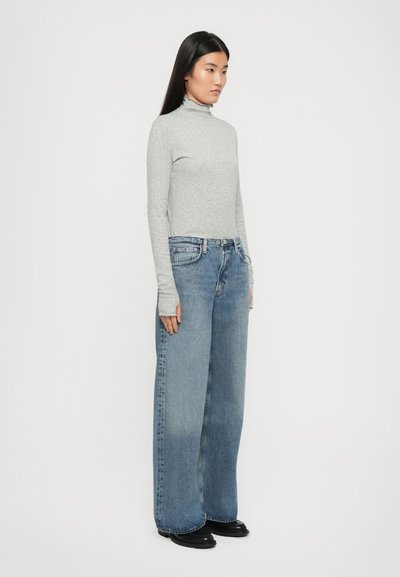 Gray long-sleeve turtleneck top paired with wide-leg blue jeans. The jeans have a classic five-pocket design and a light wash. Black shoes.