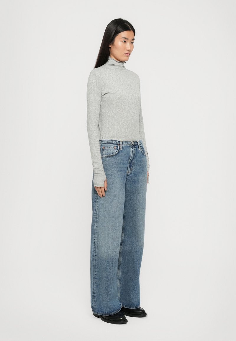 Grauer langärmeliger Rollkragenpullover kombiniert mit weit geschnittenen blauen Jeans. Die Jeans haben ein klassisches Fünf-Taschen-Design und eine helle Waschung. schwarze Schuhe.