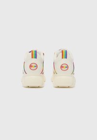 Zapatillas blancas con suela gruesa, que presentan una pestaña de talón con rayas de colores, un parche redondo con el logo y una textura suave.