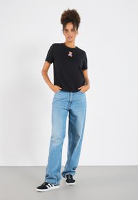 Black T-shirt with a bear graphic on the chest, paired with light blue wide-leg jeans and black sneakers with white accents.