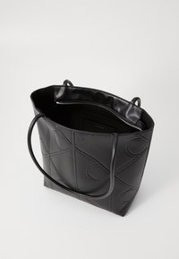Sac fourre-tout noir avec un motif embossé, fabriqué en matériau lisse. Présente des poignées doubles et un haut ouvert avec une poche intérieure zippée.