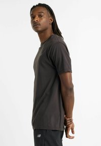 Dark gray short-sleeve t-shirt with a textured surface, crew neck, and subtle logo detail on the chest, paired with black athletic pants.