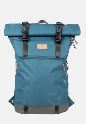 Teal-rulla reppu mustilla remmeillä ja varusteilla, nahkainen etiketti, harmaa pohja ja sivutaskut lisätoiminnallisuutta varten.