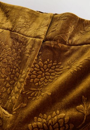 Samtstoff in einem reichen goldbraunen Farbton mit floral geprägten Mustern. Die Textur wirkt weich und plüschig, mit glatten Nähten.