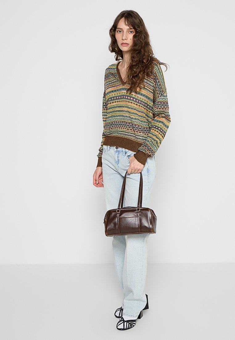 Bunt gestrickter Pullover mit V-Ausschnitt und braunen Akzenten, kombiniert mit hellblauen Jeans im geraden Schnitt und einer braunen Lederhandtasche.