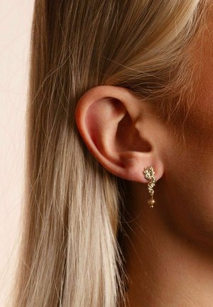 Goldene Ohrringe mit abstraktem Design, bestehend aus einem strukturierten oberen Teil und einem hängenden Perlenakzent. Leicht und modern geformt.