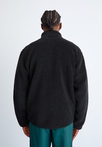 Zwart fleece sweatshirt met een gestructureerd oppervlak, hoge kraag en een comfortabele pasvorm, gecombineerd met teal broek. Zichtbare naden en geen sluitingen.