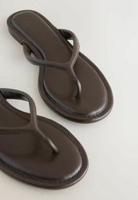 Sandales tongs en cuir brun foncé avec bouts arrondis et brides simples sur une surface claire.
