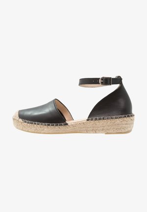 Espadrille de cuero negro con correa al tobillo, lados abiertos, suela envuelta en yute, punta redondeada y forro beige. Suela texturizada para mayor agarre.