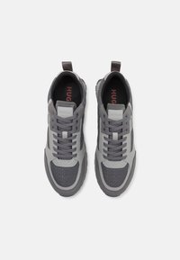 Gray sneakers featuring a mix of textured and smooth materials, with laces, a logo detail, and a patterned side panel.
