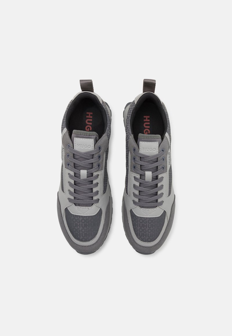 Graue Sneaker, die eine Kombination aus strukturierten und glatten Materialien aufweisen, mit Schnürsenkeln, einem Logodetail und einem gemusterten Seitenpanel.