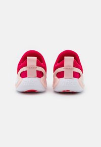 Para czerwonych i różowych sneakerów Nike pokazana od tyłu, z białymi podeszwami z napisem "nike" oraz tkaninowymi uchwytami na piętach.