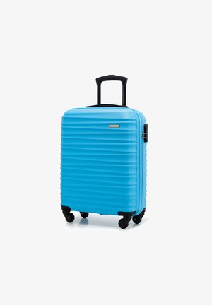 Maleta dura azul con textura acanalada vertical, ruedas negras y un asa retráctil. Cuenta con un mecanismo de bloqueo lateral.