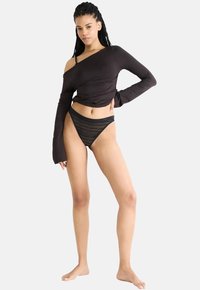 Zwarte longsleeve top met een asymmetrische halslijn, gecombineerd met een zwarte kanten string. Beide kledingstukken hebben een gladde textuur en een getailleerd ontwerp.