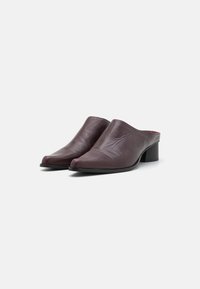Mules de piel burdeos con textura suave, punta afilada y tacón cuadrado. El diseño es minimalista sin herrajes o patrones visibles.