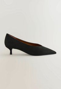 Chaussure à talon kitten en daim noir à bout pointu avec talon bas courbé et doublure intérieure marron lisse sur fond uni.