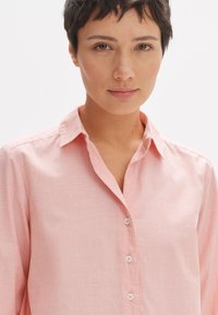 Camicia button-up rosa chiaro con collo a camicia, caratterizzata da una sottile trama e cinque bottoni coordinati lungo il davanti.
