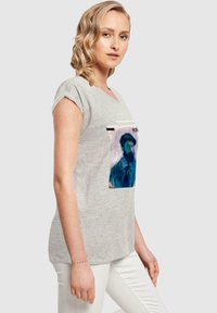 Grå kortærmet T-shirt med et frontprint af en skægget mand i blå og røde toner. V-hals design, blød tekstur, afslappet pasform.