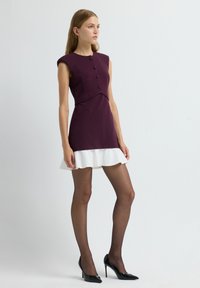 Robe sans manches violette avec des boutons décoratifs, corsage ajusté et ourlet clair blanc. Portée avec des collants noirs transparents et des talons hauts noirs.