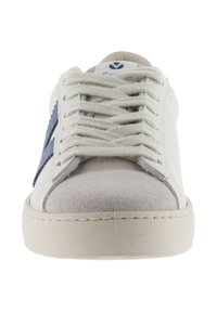 Zapatilla de piel blanca con puntera de gamuza gris clara y franja de acento azul. Cuenta con cordones planos y suela de goma. Diseño clásico de corte bajo.