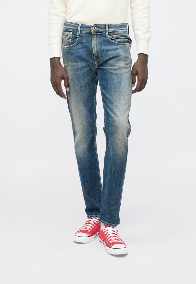 Μπλε τζιν παντελόνι με ξεθωριασμένη όψη, ευθείες γραμμές, πέντε τσέπες και φερμουάρ. Συνδυασμένο με κόκκινα πάνινα παπούτσια.