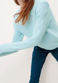 Pull tricoté bleu clair à manches longues avec un motif texturé, associé à un pantalon bleu foncé. Le pull présente un col rond.
