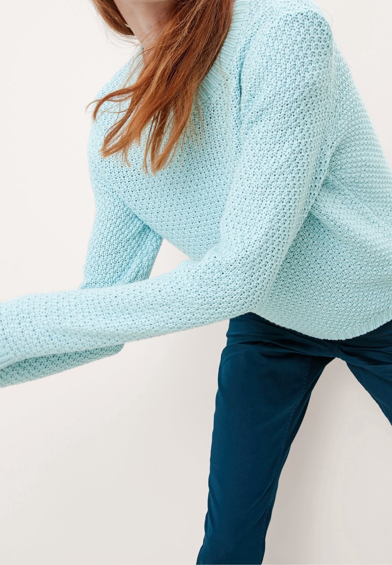 Pull tricoté bleu clair à manches longues avec un motif texturé, associé à un pantalon bleu foncé. Le pull présente un col rond.
