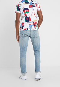 Kortärmad, vit T-shirt med färgglada mönster av segelbåtar och bojar, som är i kombination med ljusblå jeans och vita sneakers med blå detaljer.