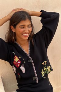 Čierny kardigán s ružovým lemovaním, s jemnou výšivkou srdiečok, rúk a kvetinových vzorov. Dvoje veľké gombíky vpredu.