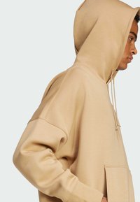 Sudadera beige con un gran bolsillo frontal, cordón ajustable y puños de canalé. Tejido suave, corte relajado y diseño oversize.