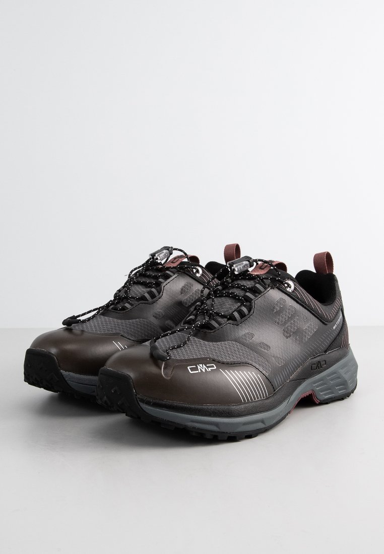 Une paire de chaussures de randonnée brunes et noires avec des semelles grises, des bandes réfléchissantes et des lacets à tirage rapide sur une surface grise uniforme.