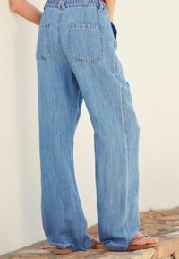 Jasnoniebieskie szerokie spodnie dżinsowe z elastycznym pasem, dwoma tylnymi kieszeniami i luźnym krojem. Tkanina ma miękką, lekko fakturowaną powierzchnię.